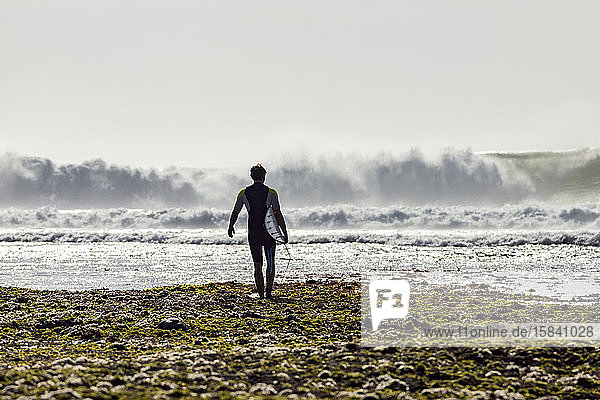 Mann mit Surfbrett beim Spaziergang am Strand