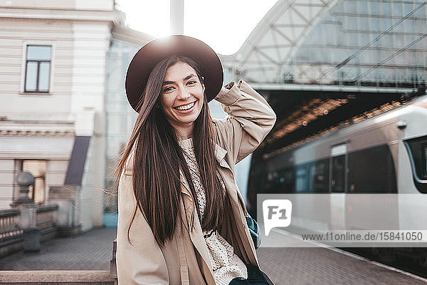 Lächelndes Mädchen mit Hut am Bahnhof wartet auf die Abfahrt des Zuges