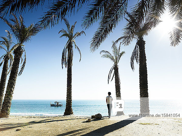 Frau beim Betrachten des Meeres zwischen Palmen am Strand von P