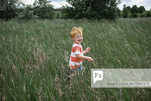 Kleinkind lacht  während es draußen durch ein langes Grasfeld läuft