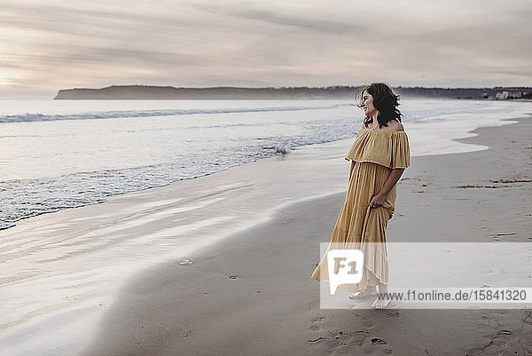 Lifestyle-Porträt einer jungen Frau  die am Strand vor bewölktem Himmel steht