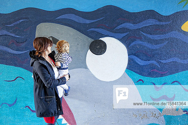 ein kleiner Junge und ihre Mutter  die an der Vorderseite einer Straßenkunst in einer Galerie in Lomener  Bretagne  Frankreich  vorbeigehen.