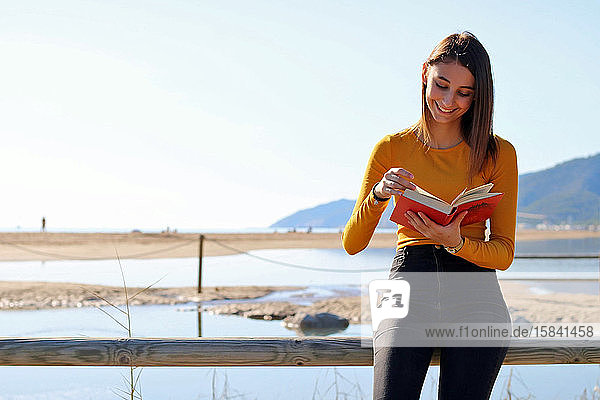Gelb gekleidetes junges Mädchen liest am Strand ein Buch.