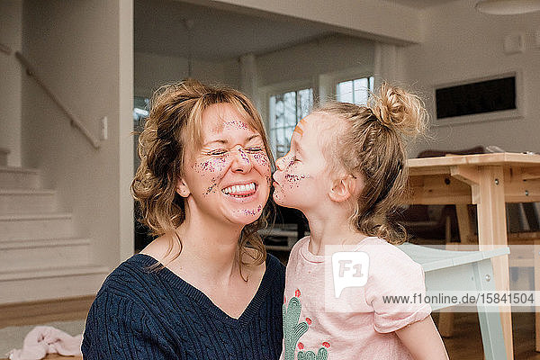 Mutter und Tochter spielen zu Hause mit Schminke und lachen zusammen