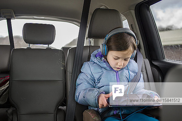 Front view of a small child in a carseat watching a tablet screen