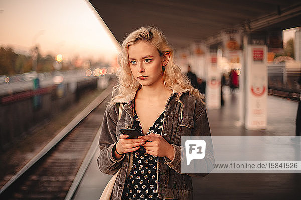 Young thoughtful woman using smart phone while waiting for train