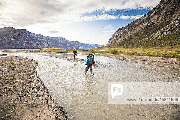 Two backpackers crossing river on Baffin Island.