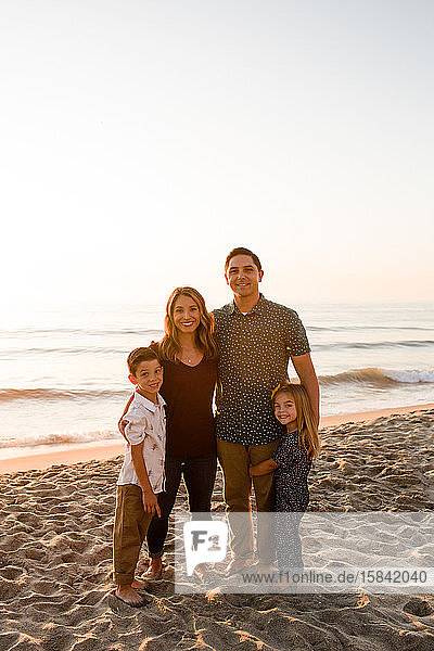 Family of Four Smiling at Camera  Embracing on Beach at Sunset