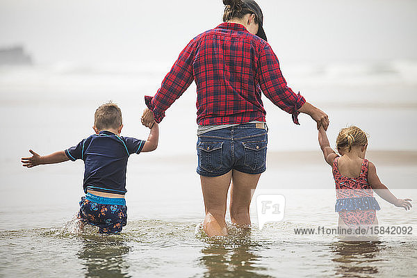 Rückansicht der Mutter  die den Kindern hilft  am Strand durchs Wasser zu waten.