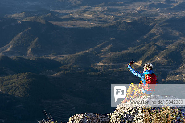 Junge Frau  die auf Felsen auf einem Berggipfel steht und ein Selfie macht.