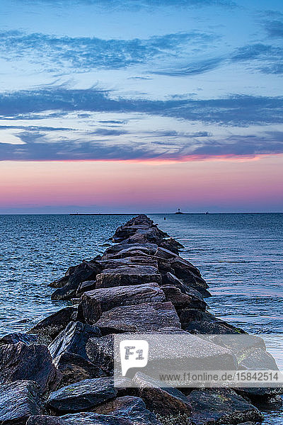 Rock pier leading out into the ocean under a pink sunset sky.