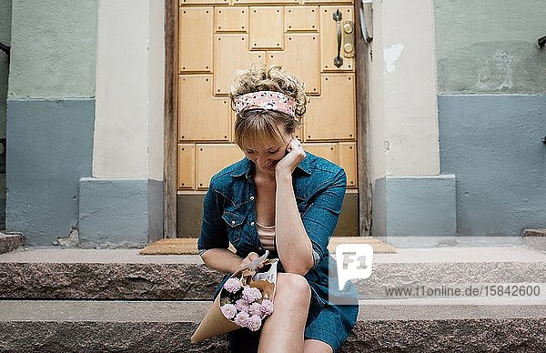 blonde Frau  die auf einer Stufe sitzt und wartet und Blumen in der Stadt hält