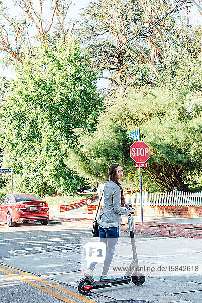 Frau überquert Straße mit Roller