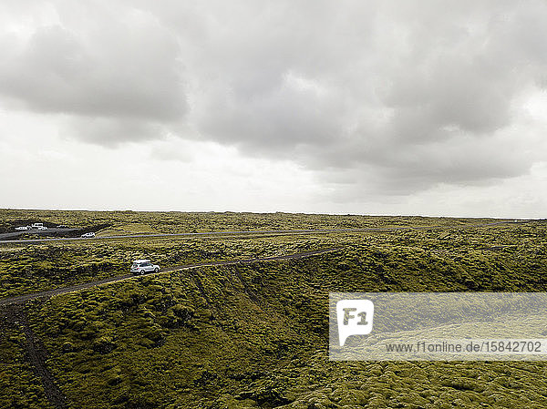 Luftaufnahme eines durch moosbedecktes Lavagestein fahrenden Autos in Ic