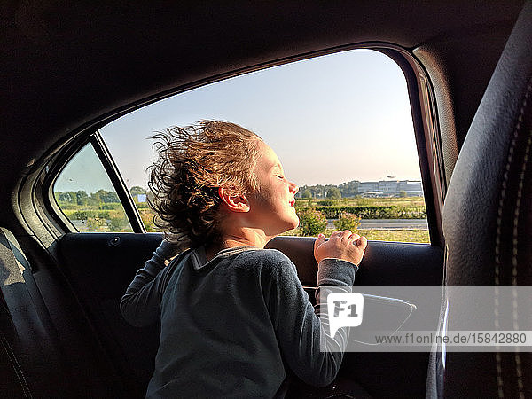 Little boy enjoying the wind in his hair while in the car