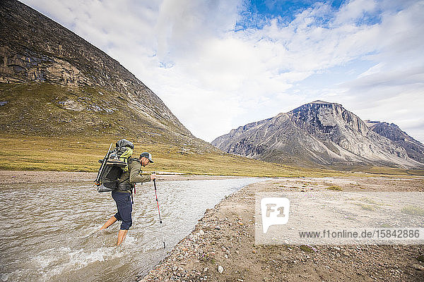 Backpacker crosses river in the arctic.