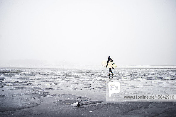 Surfer beim Spaziergang am Strand von Maine während eines winterlichen Schneesturms