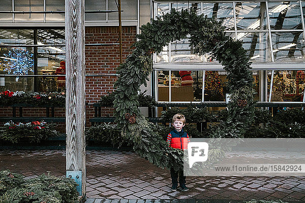 A little boy stands behind a huge wreath.