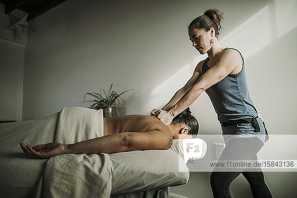 Weibliche Massagetherapeutin massiert afroamerikanischen Patienten die Schultern