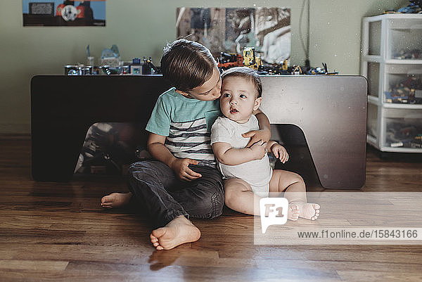 5 yr old boy holding baby sister while sitting on hardwood floor