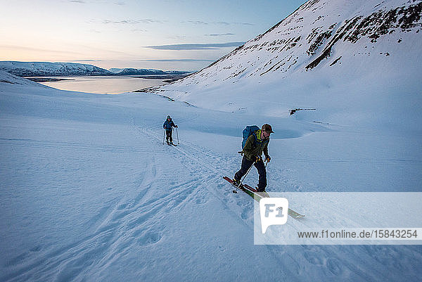Man and woman backcountry skiing in Iceland with water behind