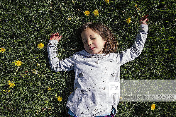 Draufsicht auf ein friedliches Kind  das im Frühling auf einem Feld mit Wildblumen liegt
