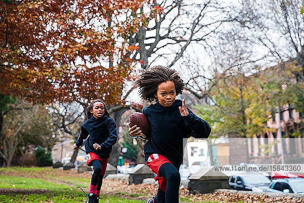 Confident girl playing American football with sister at park in city