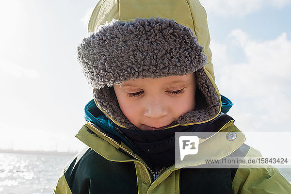 Porträt eines Jungen  der im Winter warm eingepackt am Strand liegt