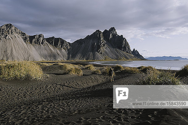 Junger Mann betrachtet dramatische Berge am Strand in Island