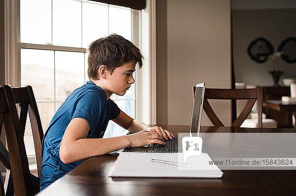 Zwischenmensch  der zu Hause auf einem Laptop an seinen Hausaufgaben arbeitet.