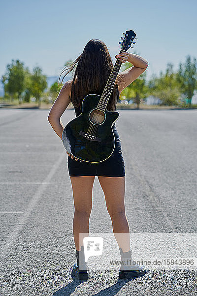 Eine jugendliche Gitarristin hält sich eine Akustikgitarre auf den Rücken.