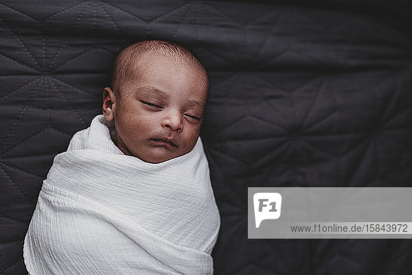 Schlafende multirassische Neugeborene  eingewickelt in eine weiße Empfangsdecke