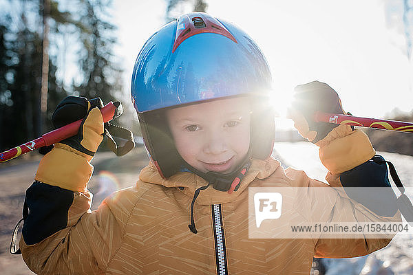 close up of a young boy wearing a ski helmet holding poles at sunset