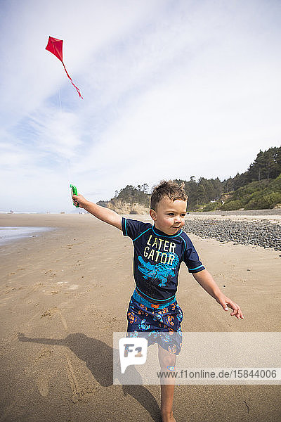 Young boy running kite along the beach with determination.