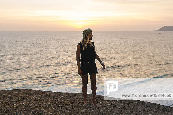 Young woman standing on rock at the beach at sunset