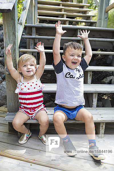 Two happy kids raise their hands in celebration  sitting on stairs.