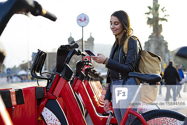 Young woman taking a rental bike with her cell phone.