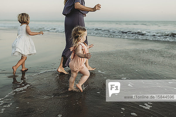 Hinteransicht einer jungen Familie  die bei Sonnenuntergang auf das Meer zugeht