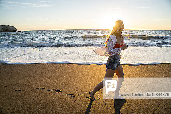 Teenager-Mädchen rennt bei Sonnenuntergang am Strand
