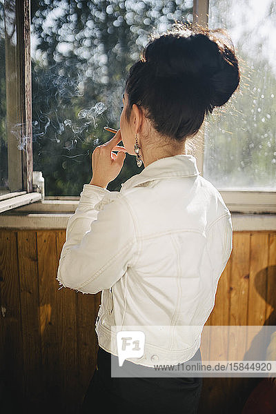 rauchende Frau auf dem Balkon mit dem Rücken stehend