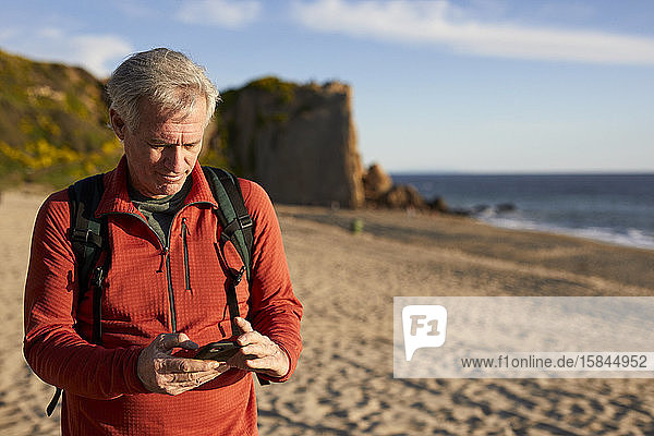 Senior man using smart phone while standing at beach during sunny day