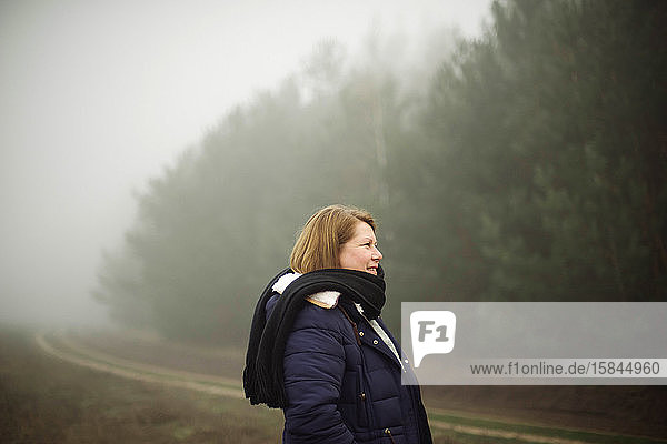 Woman standing by forest in foggy weather