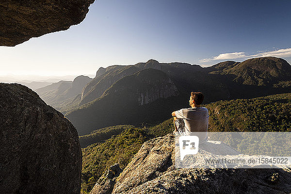 Man sitting on rocky edge looking at beautiful view to mountains