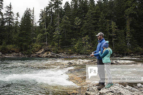 Vater und Tochter stehen auf Felsen und fischen an einem Fluss