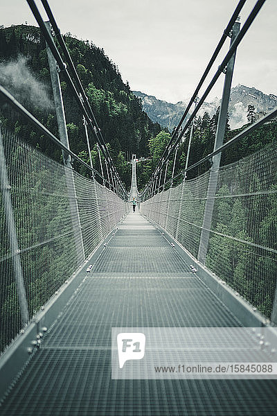Junge Frau überquert Hängeseilbrücke in alpiner Umgebung