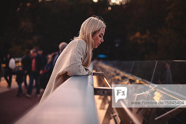 Junge Frau schaut nach unten  während sie bei Sonnenuntergang auf einer Brücke in der Stadt steht