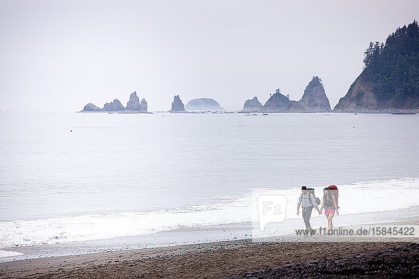 Couple walking with backpacks on Rialto Beach  Olympic National Park