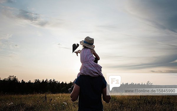 Vater trägt seine Tochter bei Sonnenuntergang auf den Schultern auf einer Wiese