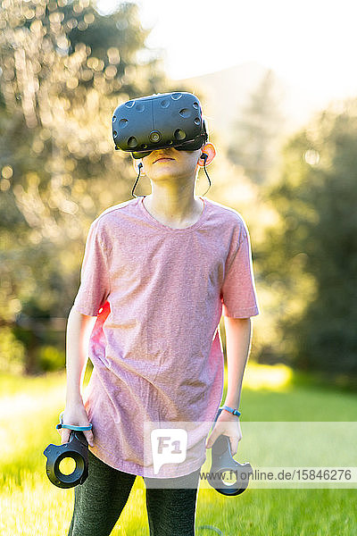 Boy standing with VR technology on while outdoors on sunny day