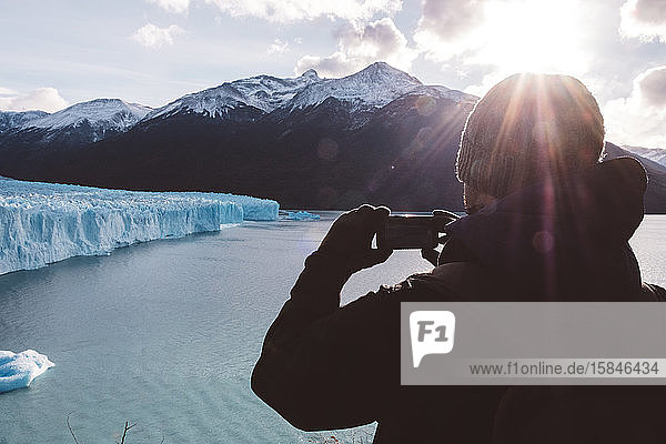 Männlicher Reisender beim Fotografieren mit einem Handy in Gletschernähe an bewölktem Tag